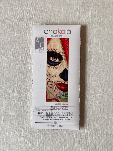 Chocolate bar in a rectangular paper package. the packaging has art of a woman with red hair wearing day of the dead face paint on the front.