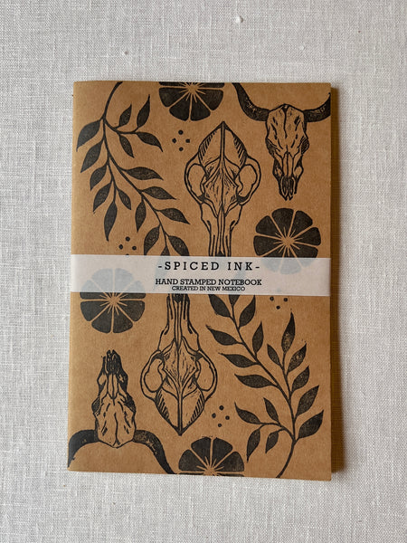Tan paper notebook with cow skulls, vines, and flowers printed in black ink.