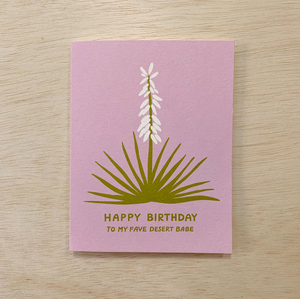 A pink happy birthday card with a yucca plant printed on it in green and white. It says Happy Birthday to My Fave Desert Babe.