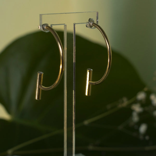 Brass semicircle earrings with closure on one end and a vertical barbell on the other end. The barbell has cubic zirconium on either side.