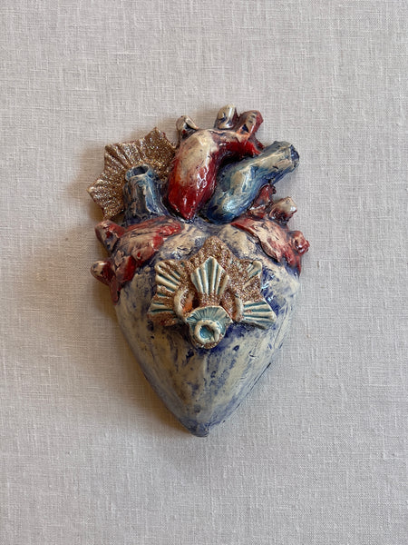 Blue anatomically correct heart  with a gold sunburst in the middle and to the left corner and red and red and blue vesicles.