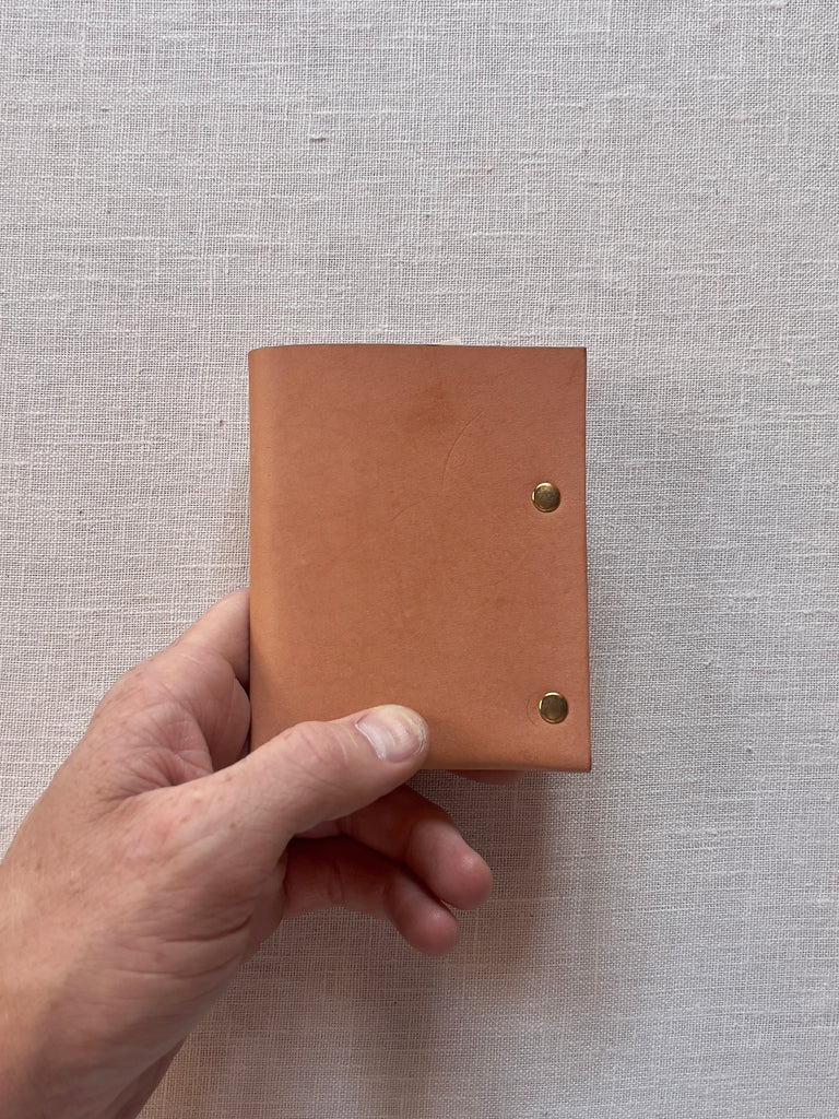 The side of a tan leather wallet with brass grommets.