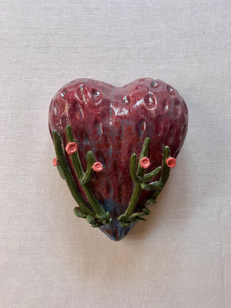 maroon heart with two cholla cactuses on either side with pink flowers atop them