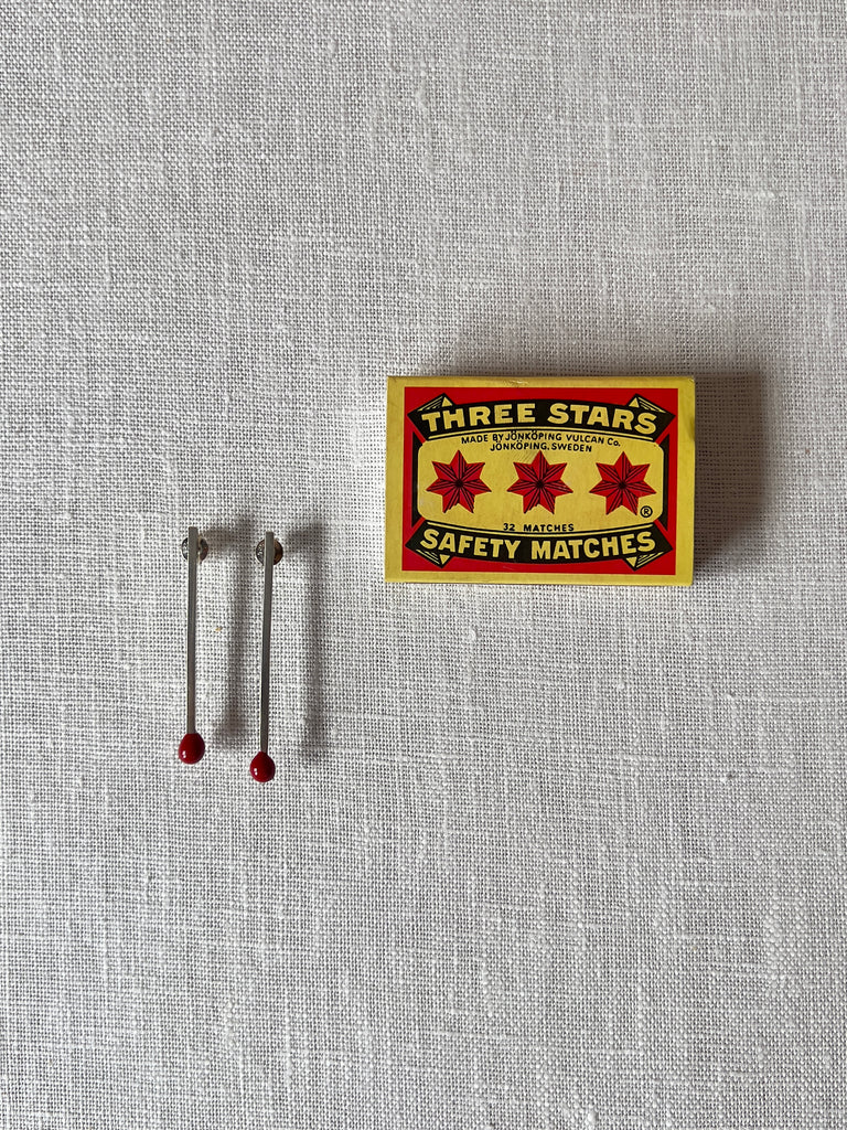 sterling silver drop earrings resembling a match with a red tip. A box resembling a match box is sitting next to them.