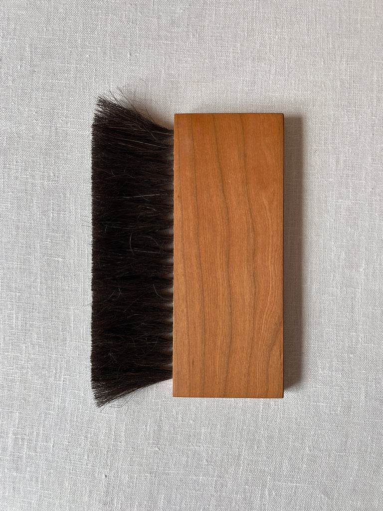 Rectangular handheld broom with rich medium brown wood and black horsehair bristles.