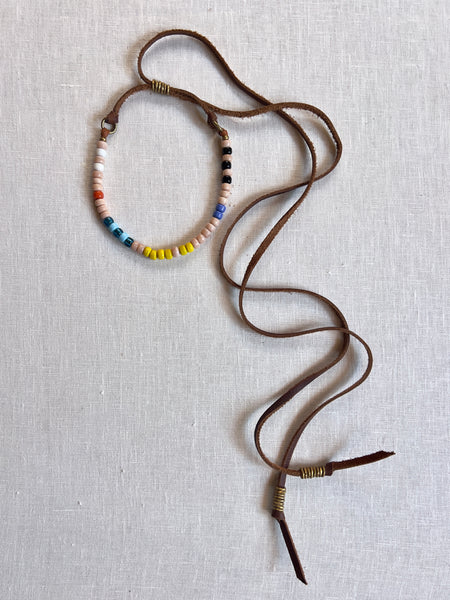 brown leather necklace with beige, blue, yellow, white, black, and orange beads. the necklace has brass coiled accents at either end.