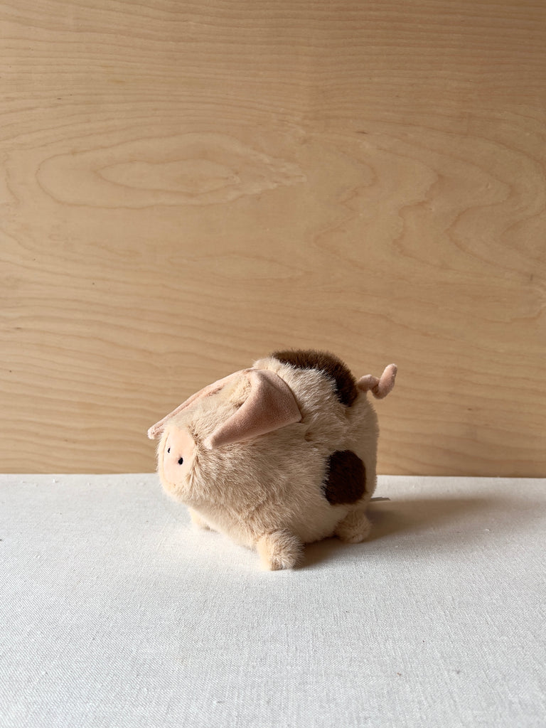 Small stuffed pink pig with brown spots. It has a large snout, small eyes, a curly tail, and triangle shaped ears.