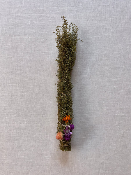 A green bundle of dried flowers with orange and purple flowers at the base