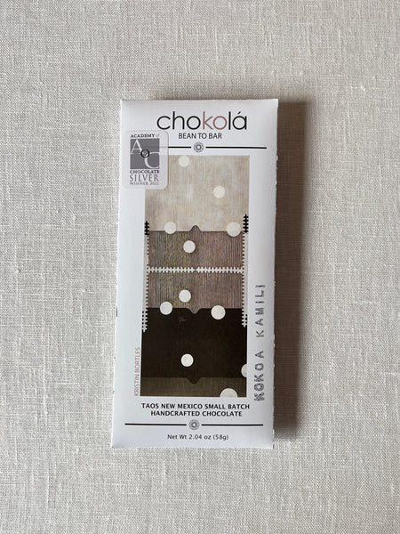 Chocolate bar in a rectangular paper package. the packaging has black and grey abstract art on the front.