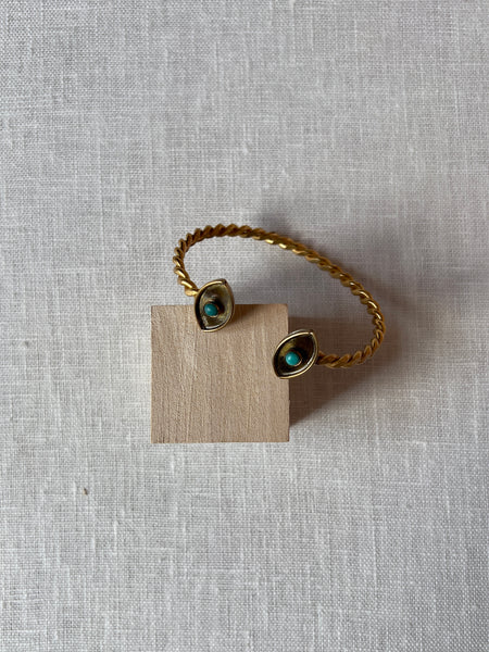 Dainty golden wrist cuff with two eyes at either end. the eyes have a greenish blue stone in the middle