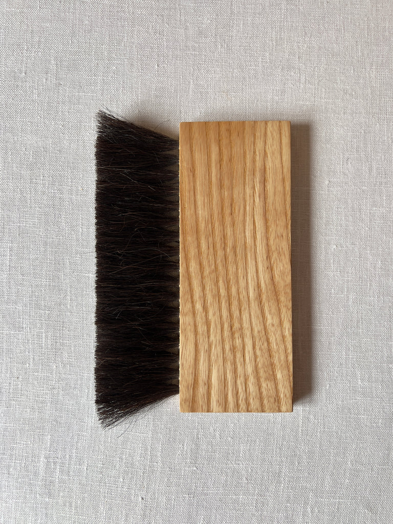 Rectangular handheld broom with light wood and black horsehair bristles.