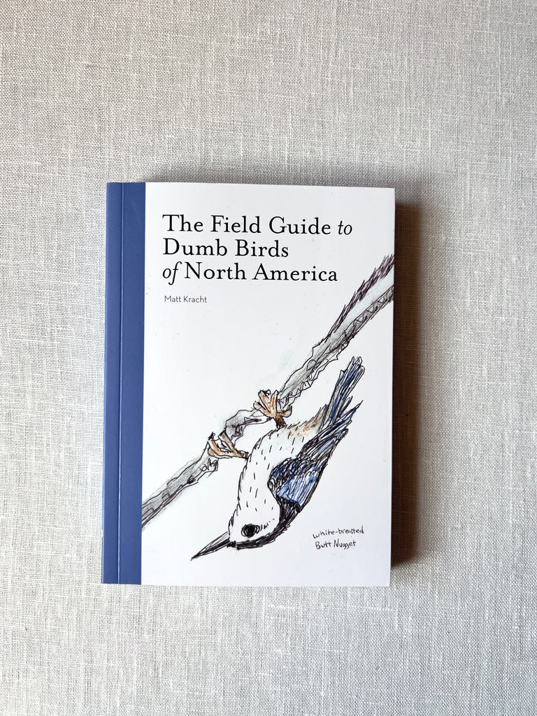 White and blue cover of the book "The Field Guide to Dumb Birds of North America" by Matt Kracht. A blue bird hanging on a branch is on the cover