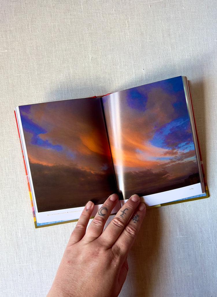 "Cloud Collectors Handbook" opened to a page with a orange, blue, and purple cloudy sunset