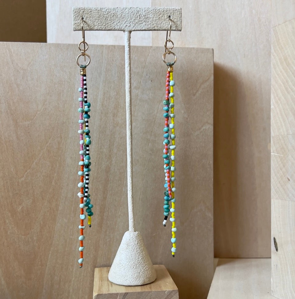 A pair of long beaded dangling earrings displayed in front of wood blocks.