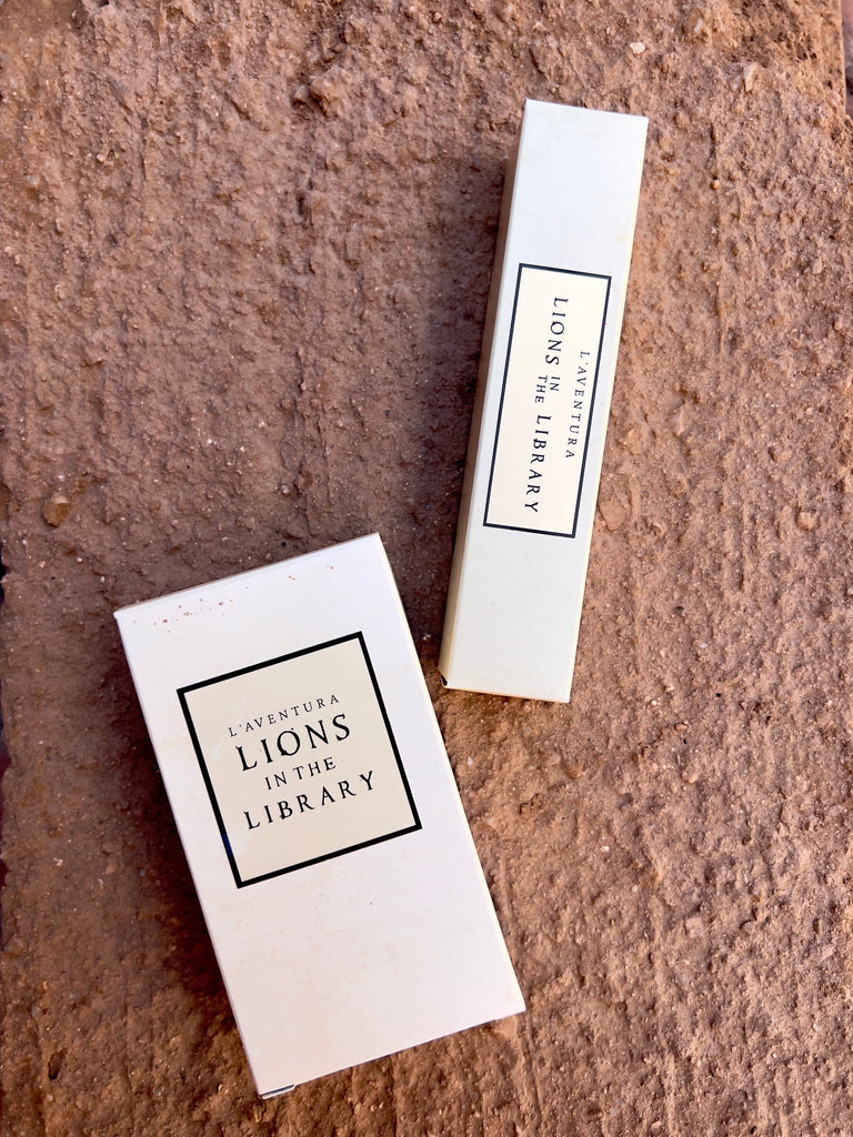Two white, rectangular paper boxes, one wider than the other. there's an off white label with a black boarder and black text in the middle of each reading "L'aventura Lions in the Library"