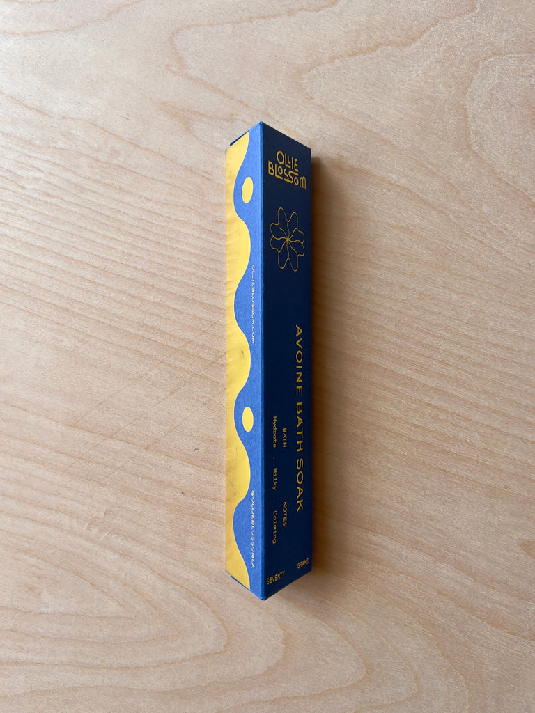 Triangular blue and gold paper packaging with gold text reading "Ollie Blossom Avoine Bath Soak."
