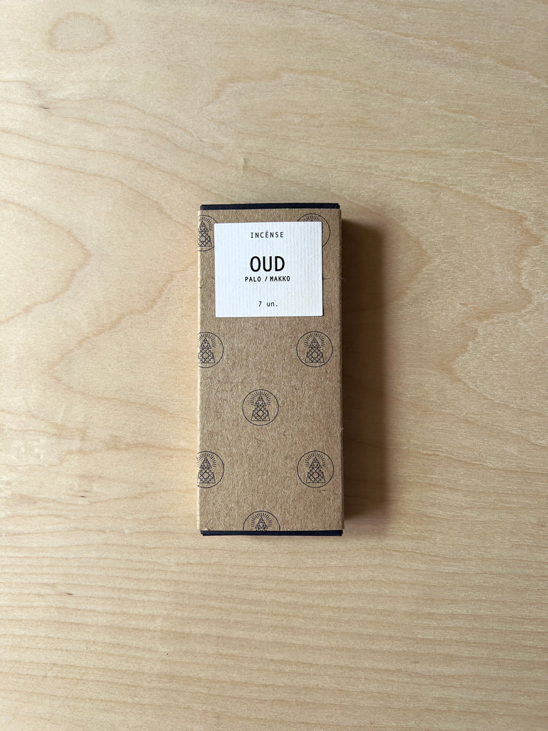 Small rectangular box of incense with two incense sticks in front of it. The incense sticks are thin, long, and hand pressed. The box has a label that reads "Oud."