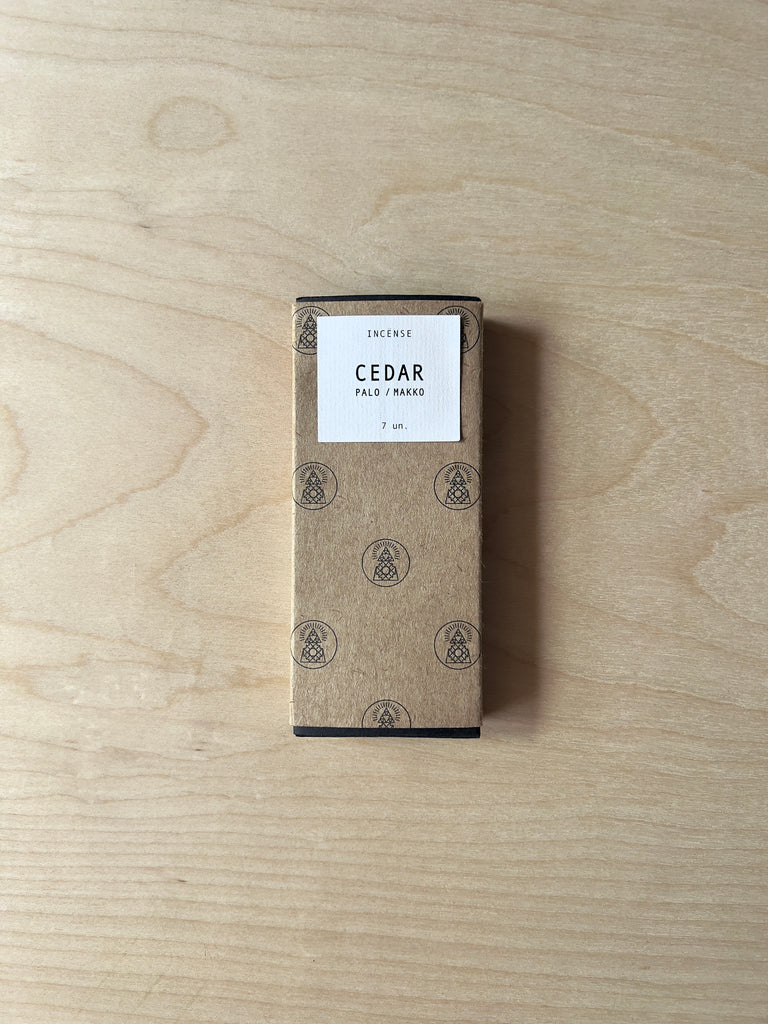 Small rectangular box of incense with two incense sticks in front of it. The incense sticks are thin, long, and hand pressed. The box has a label that reads "Cedar."