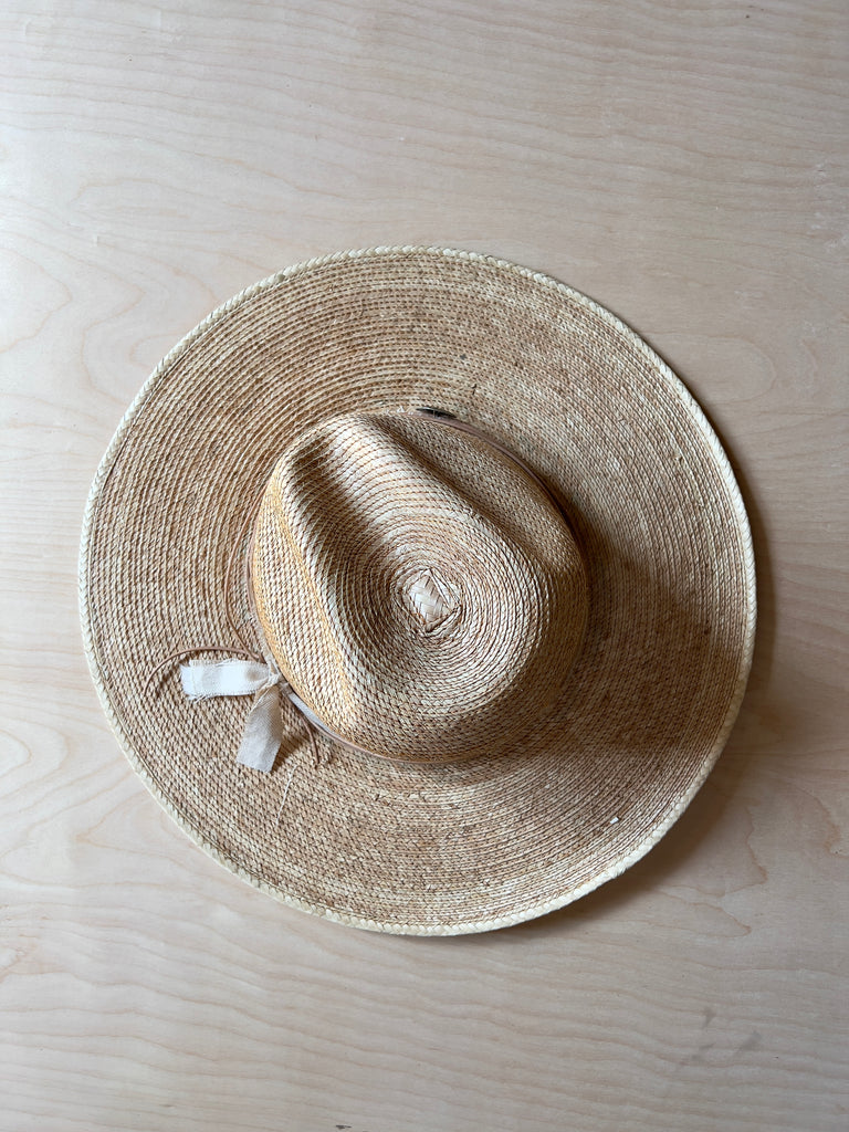 Top down view of a hand woven flat brim hat with a leather and linen hat tie and a large stylized metal bead