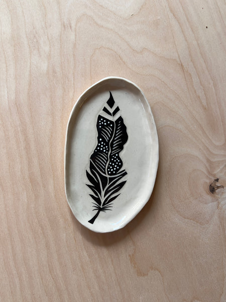 Oval ceramic dish with a black and white feather in the middle.