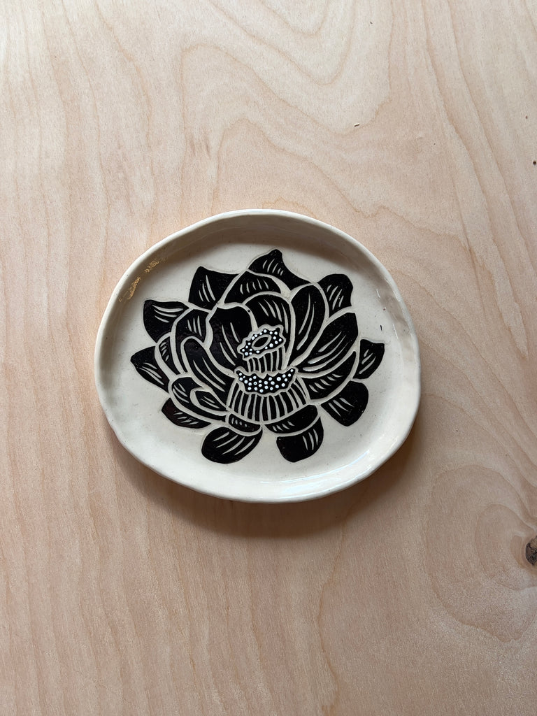 White circular ceramic dish with a stylized black and white flower resembling an opened rose.