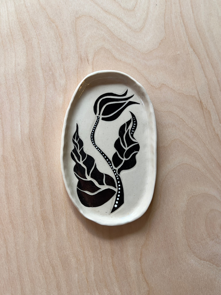 White oval ceramic dish with a black and white flower resembling a tulip with leaves.