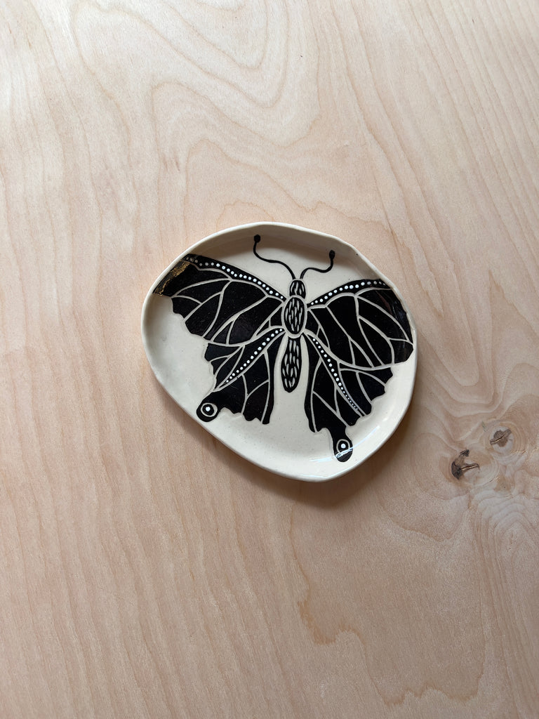 Circular ceramic dish with a black and white butterfly in the middle.