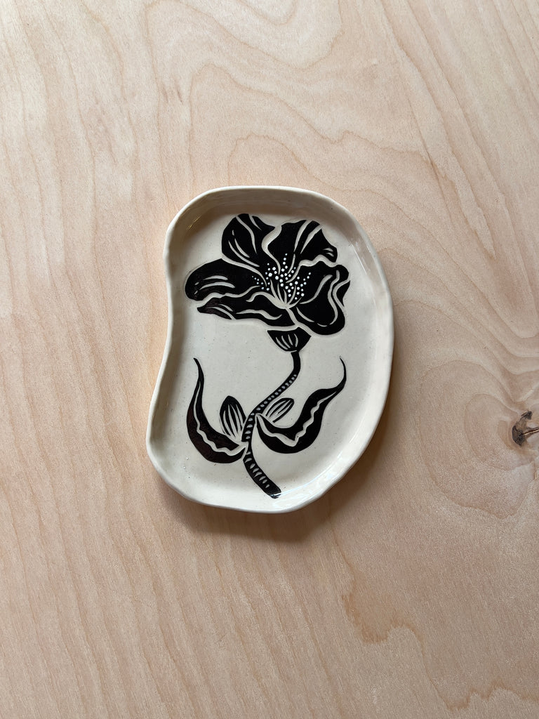White oval ceramic dish with a black and white flower in the middle resembling an opened rose with a stem and leaves.