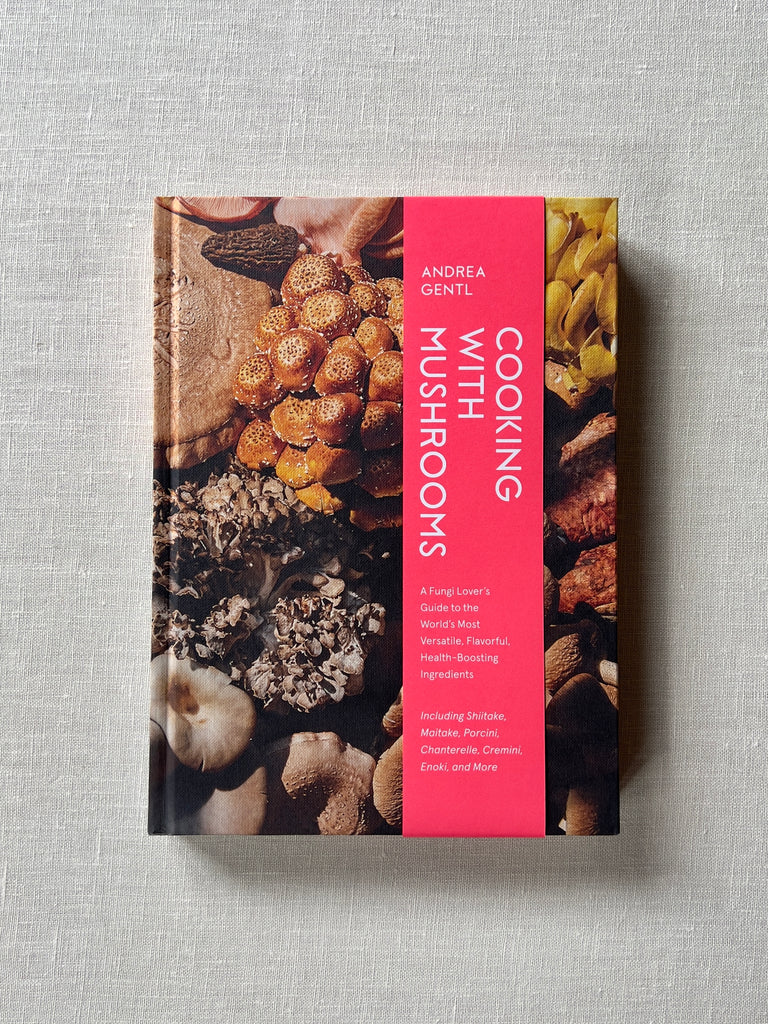 Cover of the book " Cooking With Mushrooms" by Andrea Gentl. The cover has various mushrooms broken up by a pink rectangle with white text that reads "Cooking With Mushrooms: A Fungi Lover's Guide to the World's Most Versatile, Flavorful, Health-Boosting Ingredients." "Including Shitake, Maitake, Porcini, Chanterelle, Cremini, Enoki, and More."