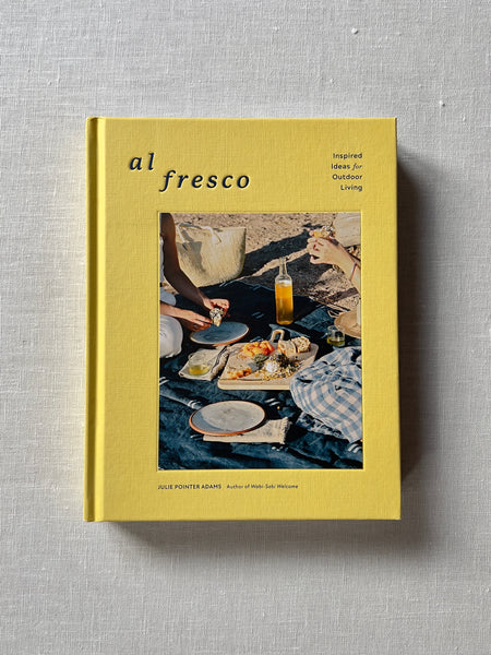 Cover of the cookbook "Al Fresco" by Julie Pointer Adams. The cover is yellow with a photo of two people sitting on a picnic blanket on a beach surrounded by food and drinks. Additional text reads "Inspired Ideas for Outdoor Living."
