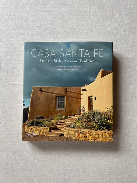 Cover of the book "Casa Santa Fe: Design, Style, Arts, and Tradition" by Melba Levick. Theres an adobe house behind the white title text.
