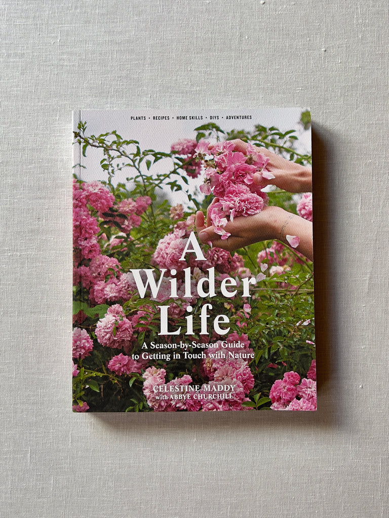 Cover of the book "A Wilder Life" by Celestine Maddy. The cover depicts a pink flower bush. Additional text reads "A Season-by-Season Guide to Getting in Touch with Nature." "Plants - Recipes - Home Skills - DIYS - Adventures."