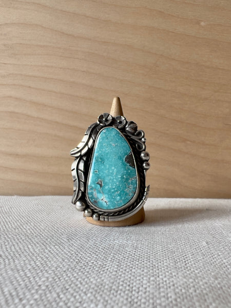 Oval shaped sterling ring with turquoise stone and flowers and feathers in sterling silver around the stone