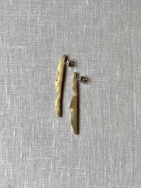 Two long brass earrings in the shape of an abstract mountain horizon, the earrings sit vertically.