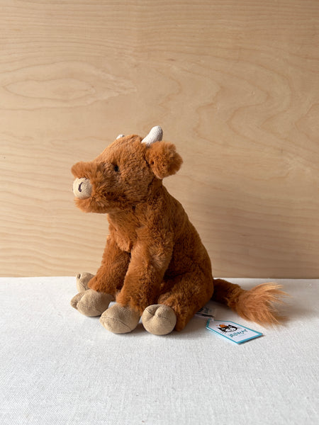 A small stuffed highland cow. The cow is auburn brown with a tan nose, horns, and hooves.