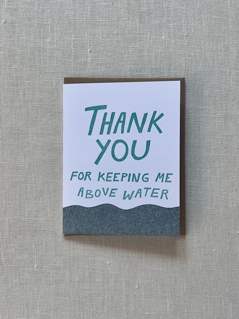 White card with blue text reading "Thank you for keeping me above water" with a body of water at the bottom of the card