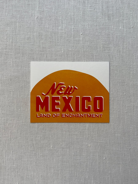 White card with a yellow half circle and red text reading "New Mexico Land of Enchantment."