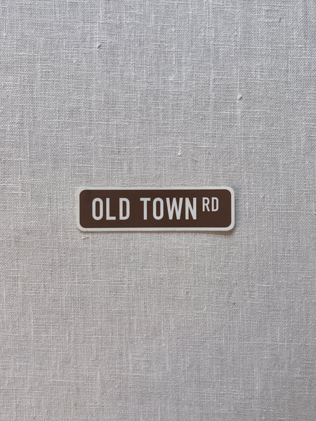 Brown rectangular sticker with white boarder and white lettering reading "old town rd"