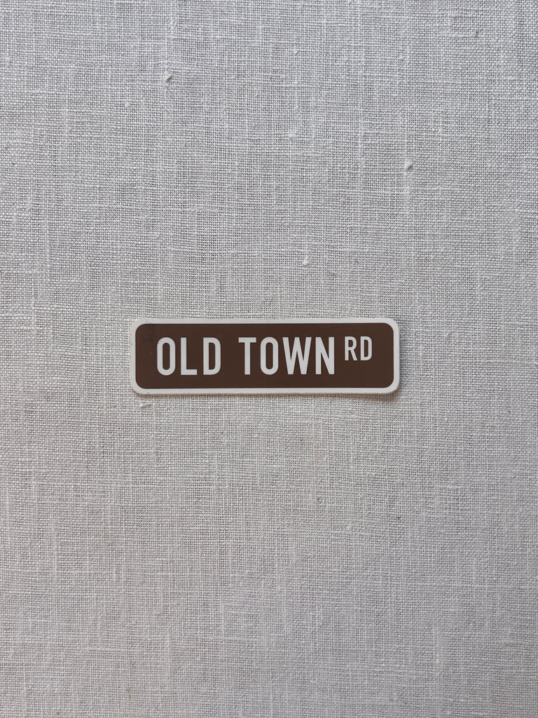 Brown rectangular sticker with white boarder and white lettering reading "old town rd"