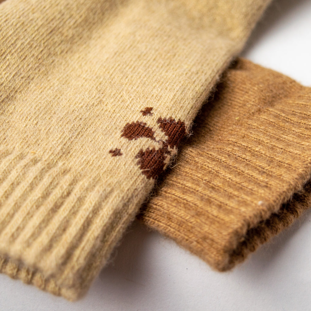 Closeup of one dark tan sock and one light tan sock on top of one another. The cuffs of the socks are ribbed and there are dark brown geometric shapes woven in at the back.