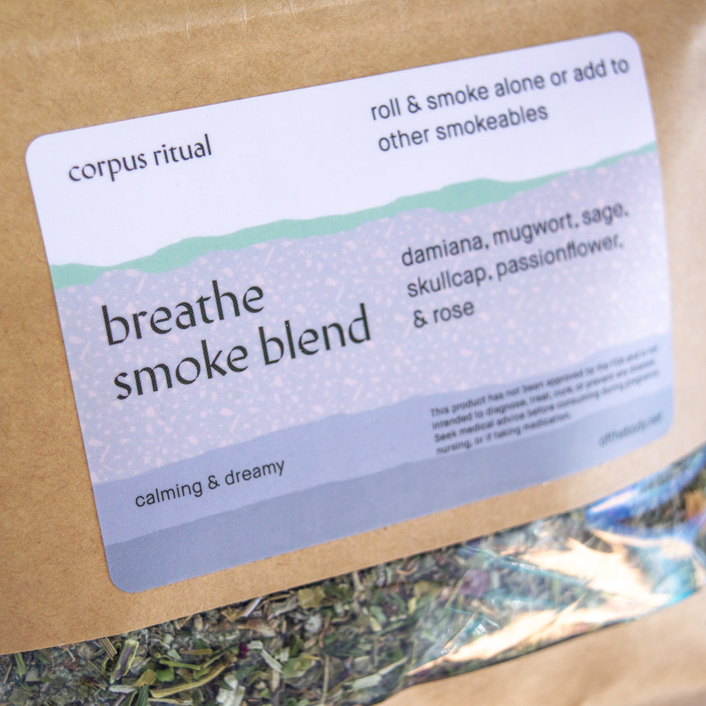 Paper bag with a clear lining nearing the bottom and a rectangular label in the middle. The label is white and blue and had black text reading "Corpus Ritual" "roll & smoke alone or add to other smokeables" "Breathe smoke blend" "damiana, mugwort, sage, skullcap, passionflower, & rose" "calming &dreamy." the clear lining shows the herbs listed before packed in the paper packet