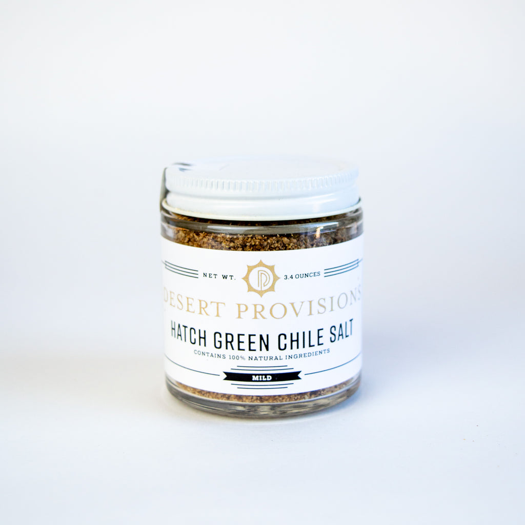Glass container with a white top and white label. the label reads " desert provisions, hatch green chile salt contains 100% natural ingredients"