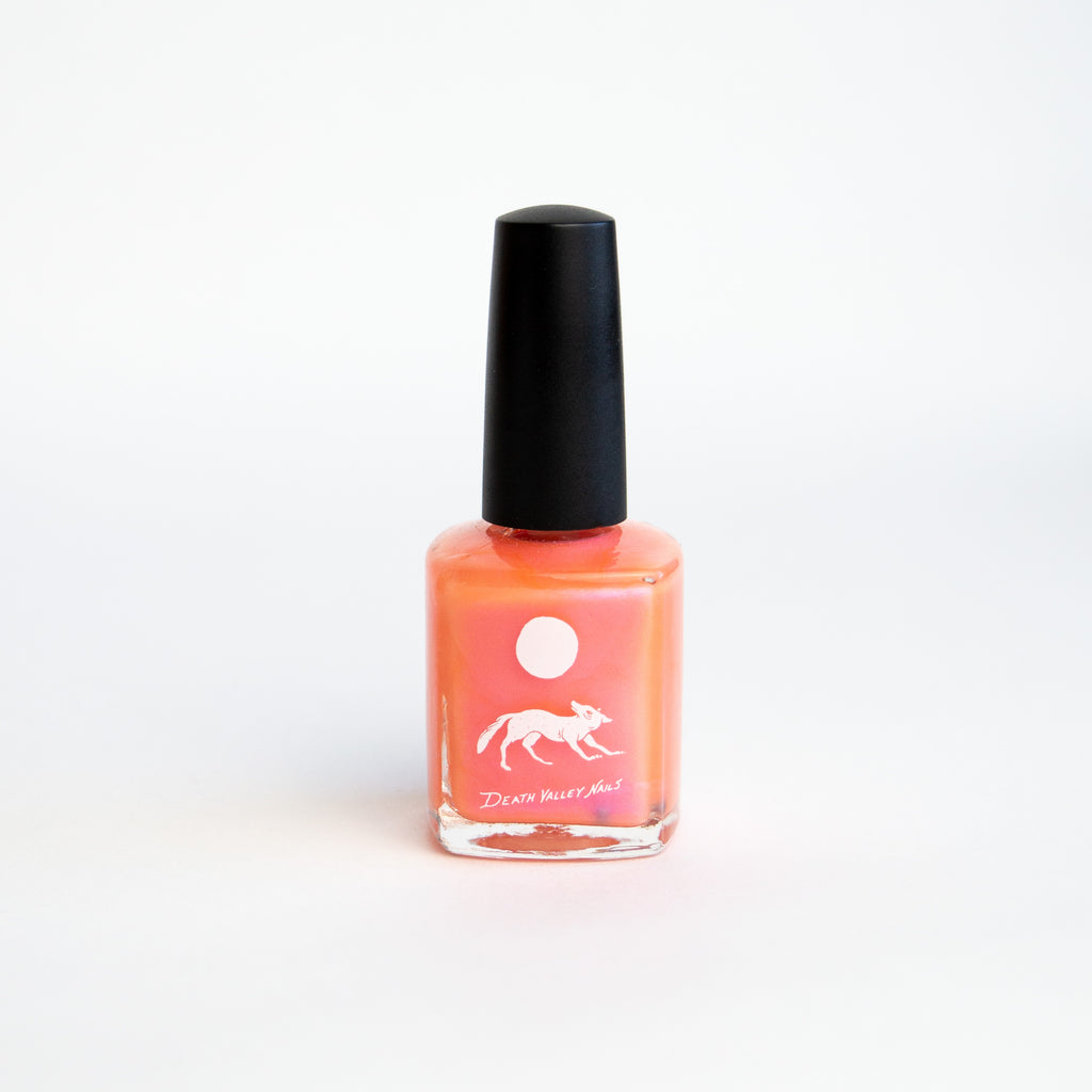 iridescent pink and orange nailpolish in a glass bottle with a black top. theres a white label with a coyote under a full moon and lettering reading "death valley nails."