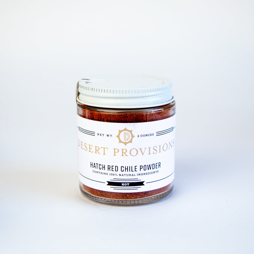 Glass container with a white top and white label. the label has gold and black text reading "desert provisions hatch red chile powder. contains 100% natural ingredients."