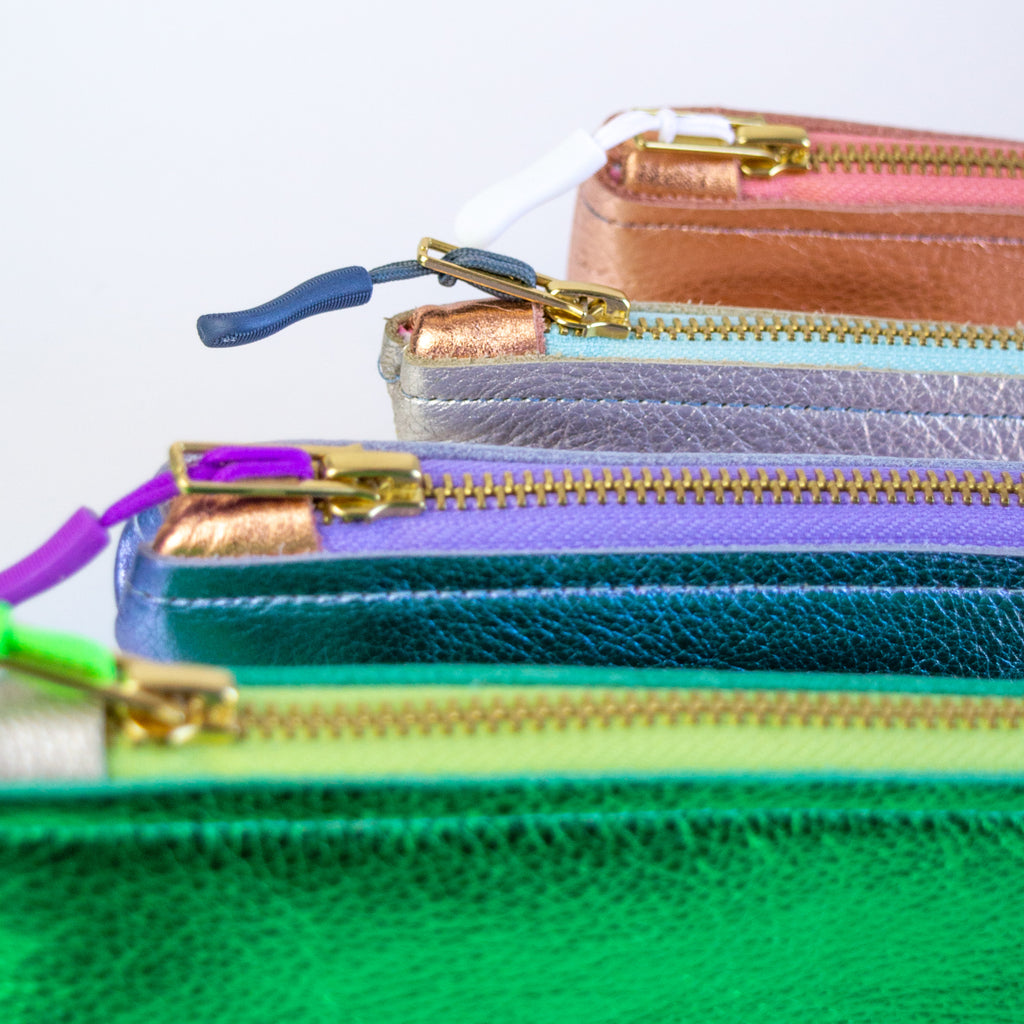 Four medium metallic pouches. From back to front: Pink, silver, purple, and green.
