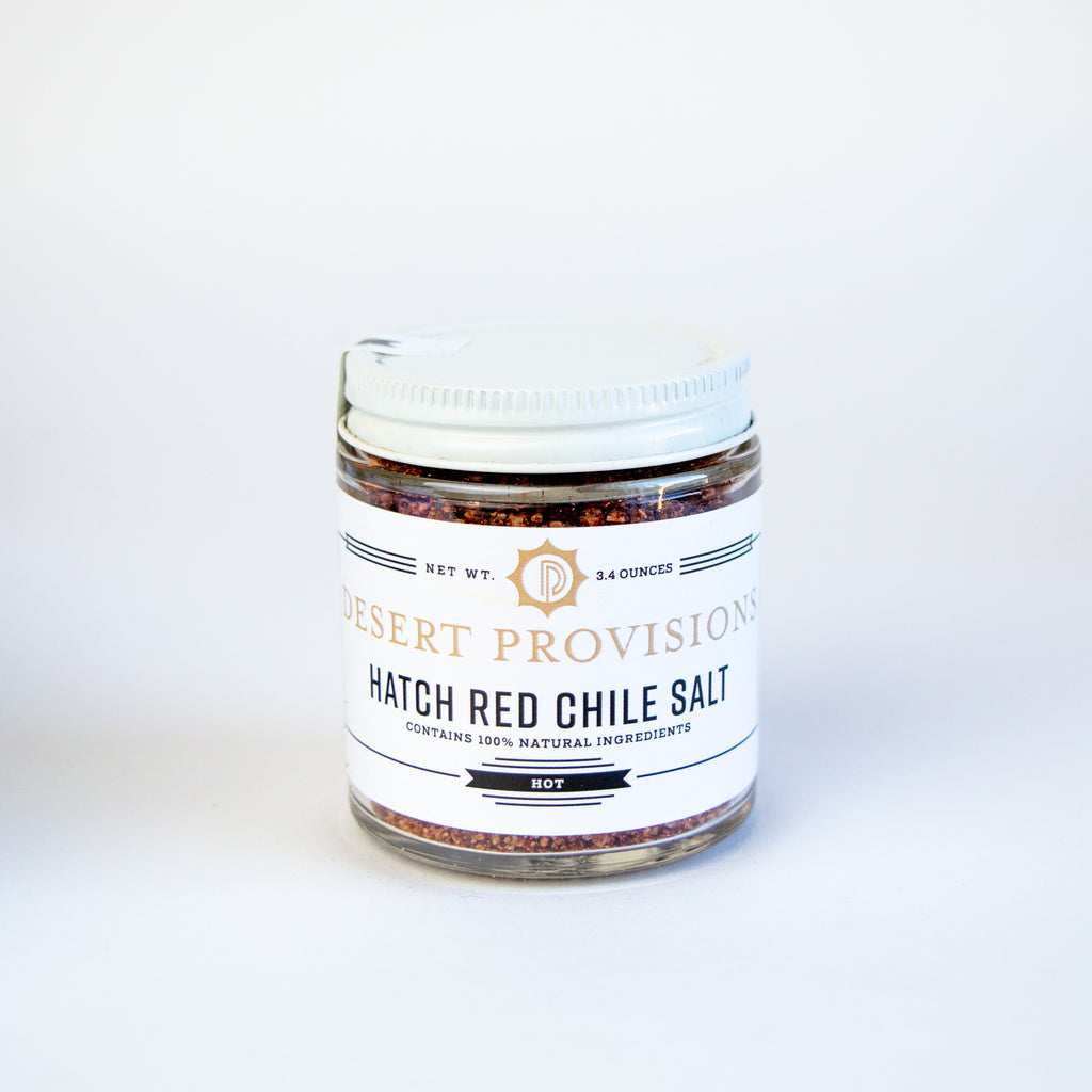 Glass container with a white top and white label. the label reads " desert provisions, hatch red chile salt contains 100% natural ingredients"