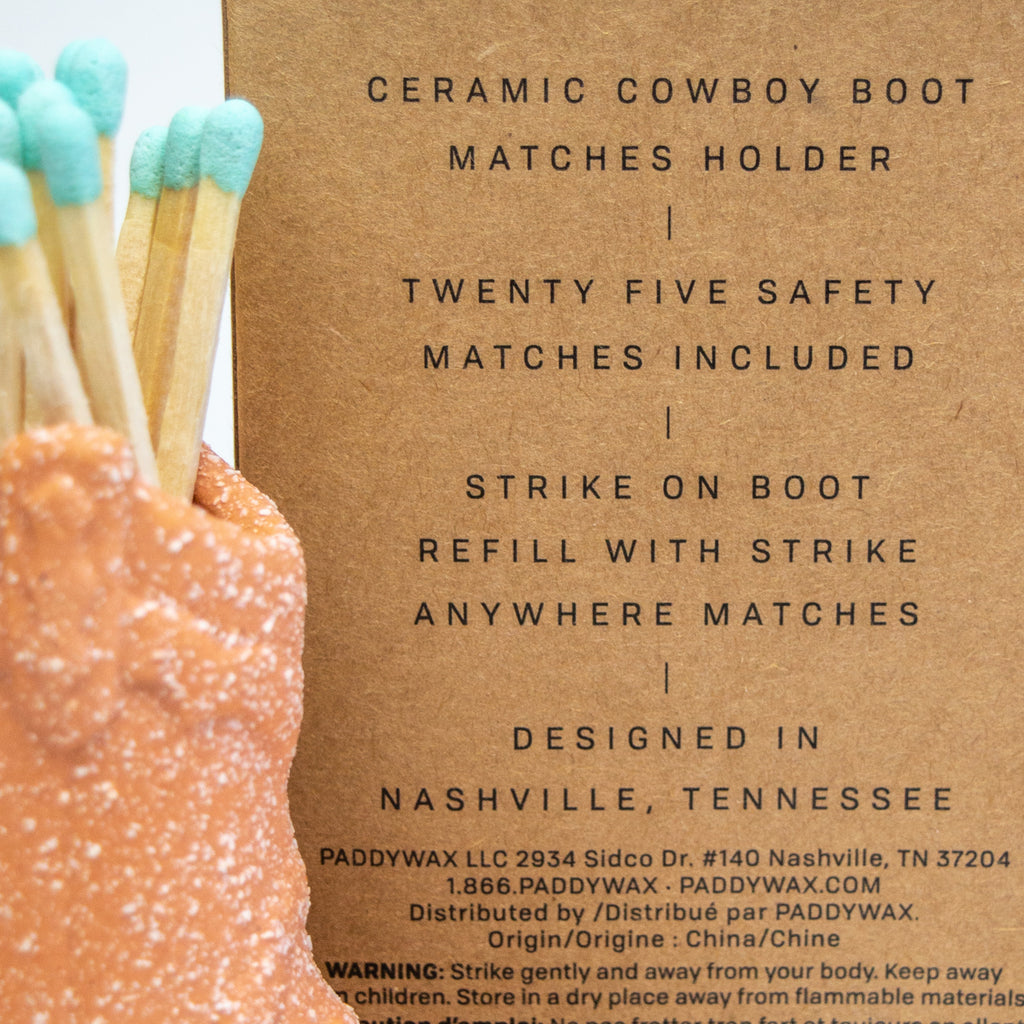 Closeup of a cardboard box showcasing black text that reads "Ceramic cowboy boot matches holder" "twenty five safety matches included" "strike on boot refill with strike anywhere matches" "designed in Nashville, Tennessee"