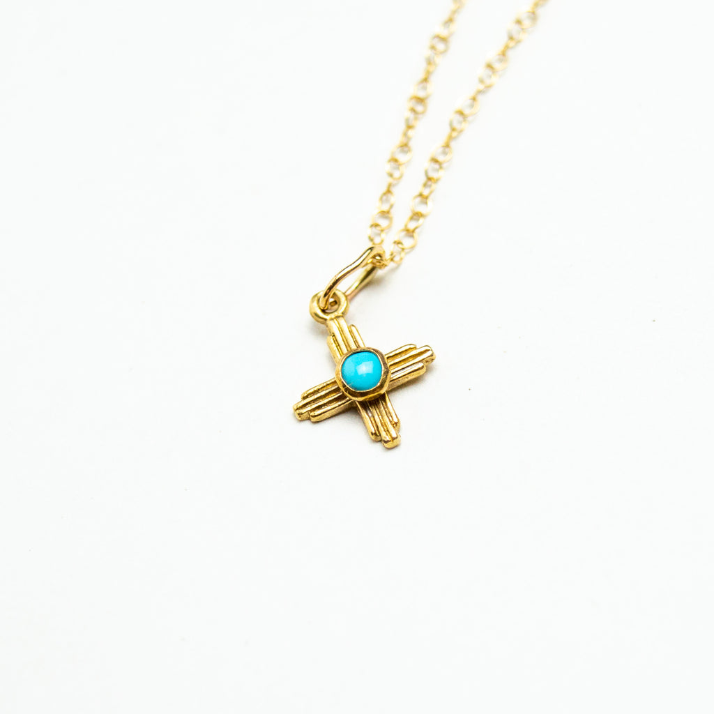 Golden zia pendant with circular turquoise stone in the middle, the pendant hangs off a golden chan with small links.