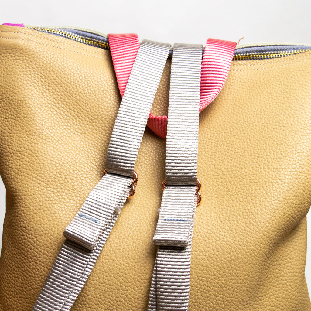 Patchwork backpack  with a tan base, silver straps and a pink handle.