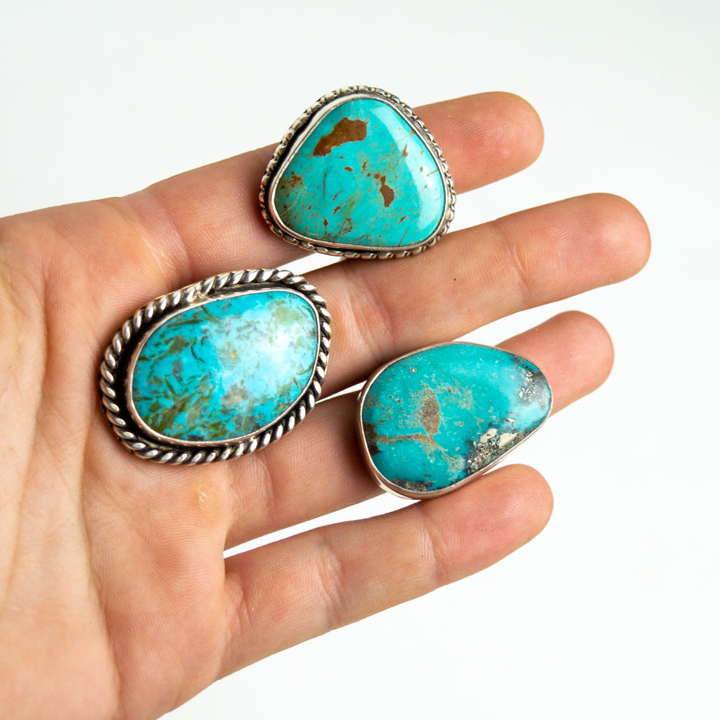 A hand holding three large turquoise and silver rings.